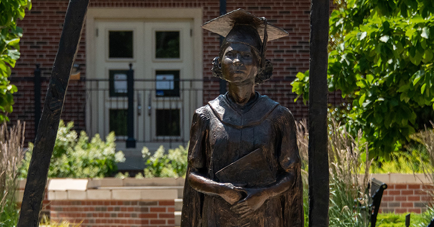 A bronze statue of a young Black woman wearing graduation regalia 